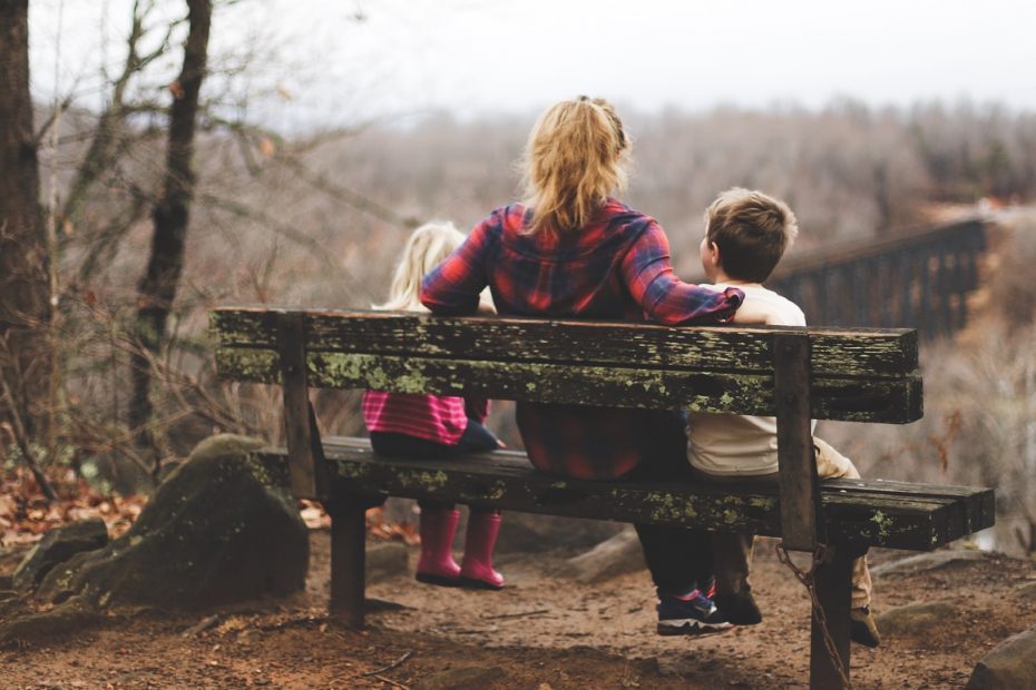 woman between two childrens sitting on brown wooden bench during daytime